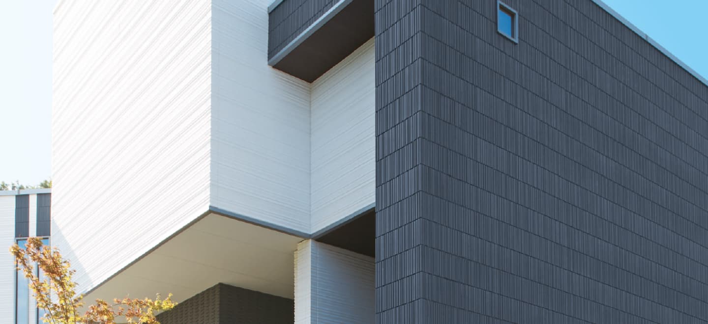 Современное здание с фасадными панелями NICHIHA Здание, облицованное оригинальными фасадными панелями из Японии от компании NICHIHA, известной своими технологичными решениями. Панели обладают наногидрофильным покрытием и функцией самоочистки, что обеспечивает долговечность и эстетичность фасада. Технология бесшовного монтажа придаёт зданию современный вид.